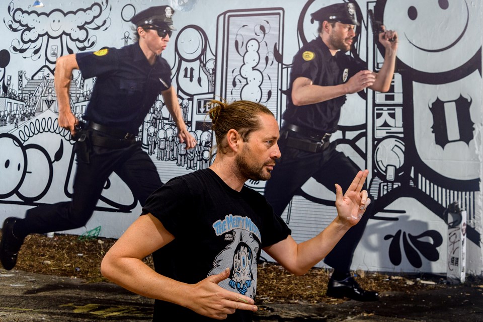 Fordoblingens kunst. Chaz Barrissonn - den ene del af street art duoen London Police - her iscensat foran Søren Solkærs portræt af duoen. Som i sine øvrige portrætter har Solkær arrangeret kunstnerne, så de indgår i sammenspil med deres egne værker. Til dette portræt lejede han politiuniformer i USA, der selvfølgelig kom med ægte pistoler. Foto: Nicholas Cho Meier Birgitte Sonne Kristensen Foto: Nicolas Cho Meier